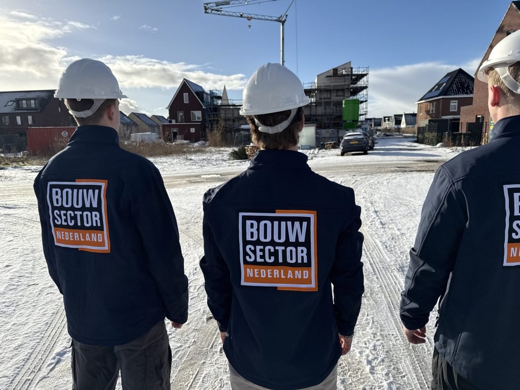 Drie vakmensen van Bouwsector Nederland met witte helm op een besneeuwde bouwplaats met een hijskraan
